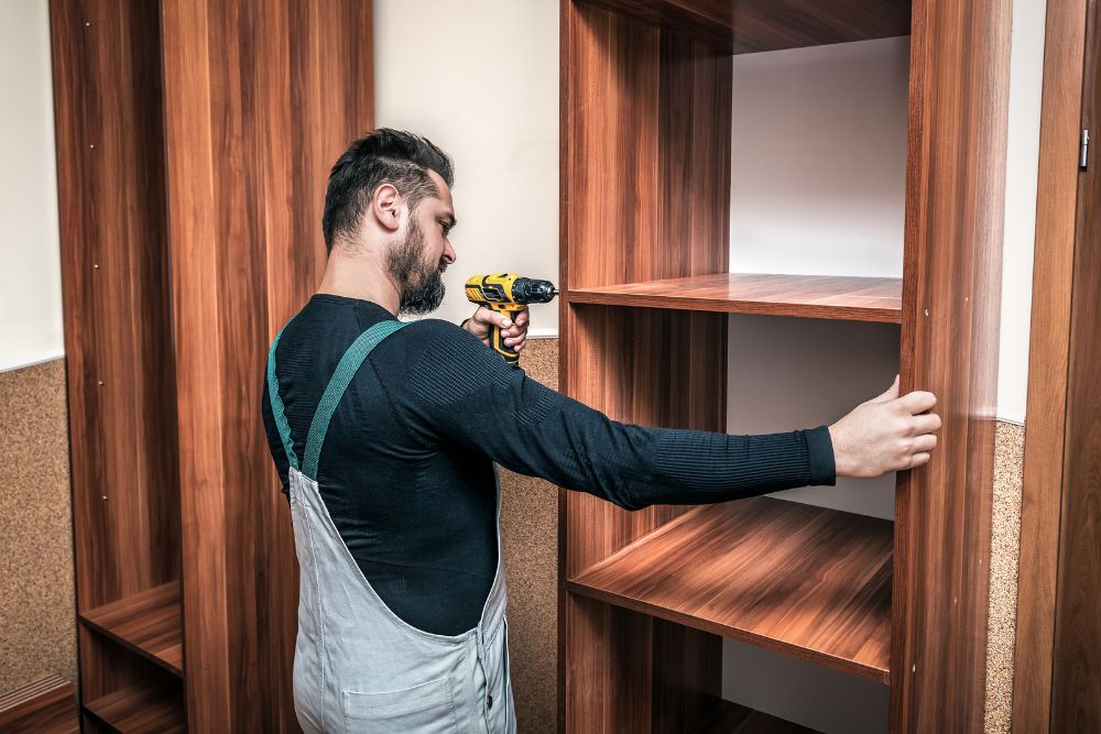 A man carefully assembles a wooden cabinet, demonstrating skill and attention to detail in a workshop setting.
