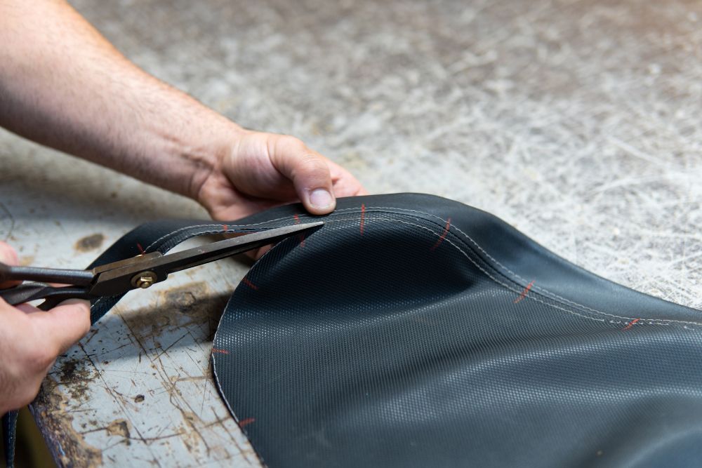 A man uses scissors to cut a leather seat, focusing intently on his task.