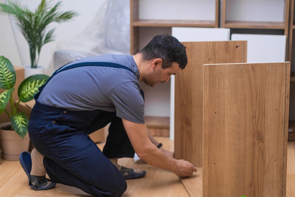 A man wearing overalls is diligently working on constructing a wooden cabinet in a workshop.