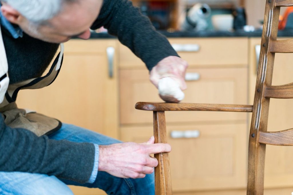 A man carefully sands a wooden chair, focusing on smoothing its surface for a polished finish.