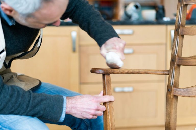 A man carefully sands a wooden chair, focusing on smoothing its surface for a polished finish.