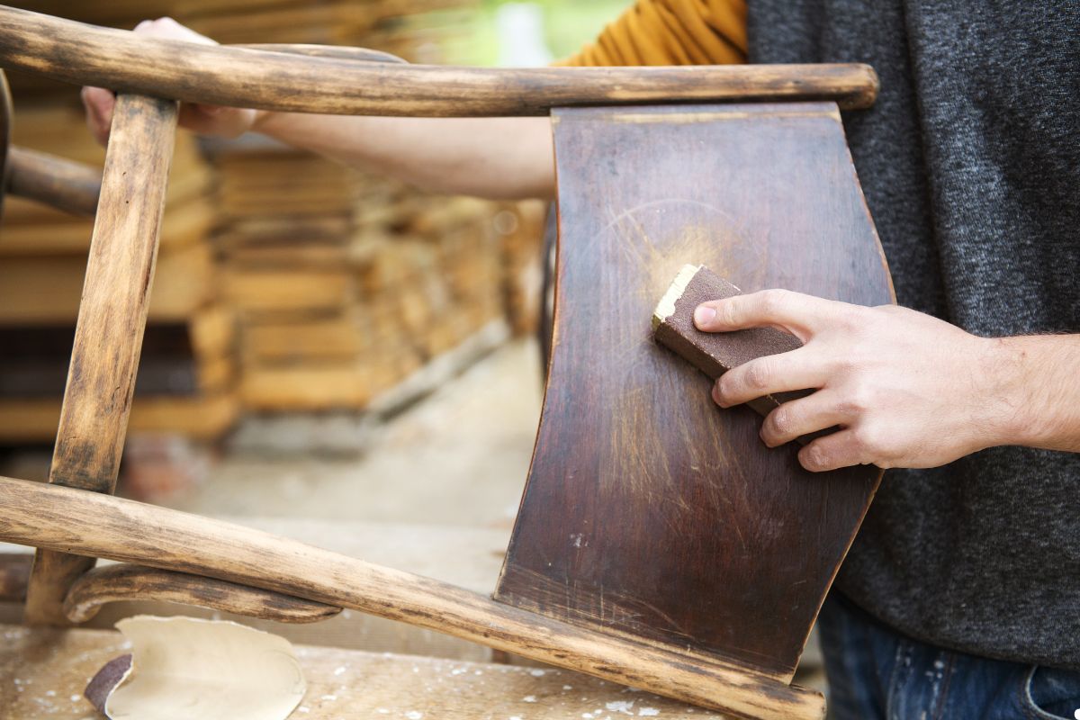 A man crafts a chair using a wooden piece, focused on his work in a well-lit workshop.