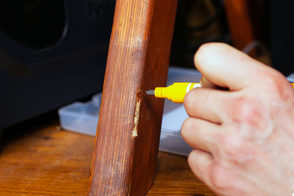 A person applies a yellow marker to touch up a wooden chair, focusing on a damaged area to restore its appearance.