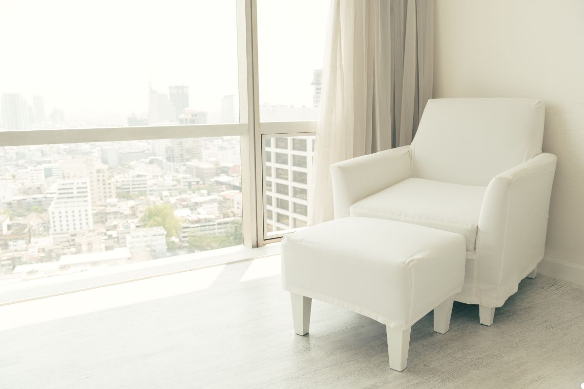 A white chair and foot stool positioned in front of a large window, allowing natural light to fill the space.
